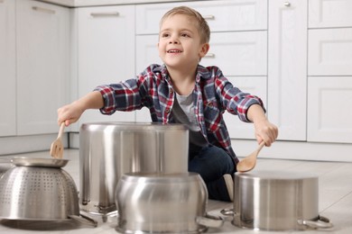 Little boy pretending to play drums on pots in kitchen