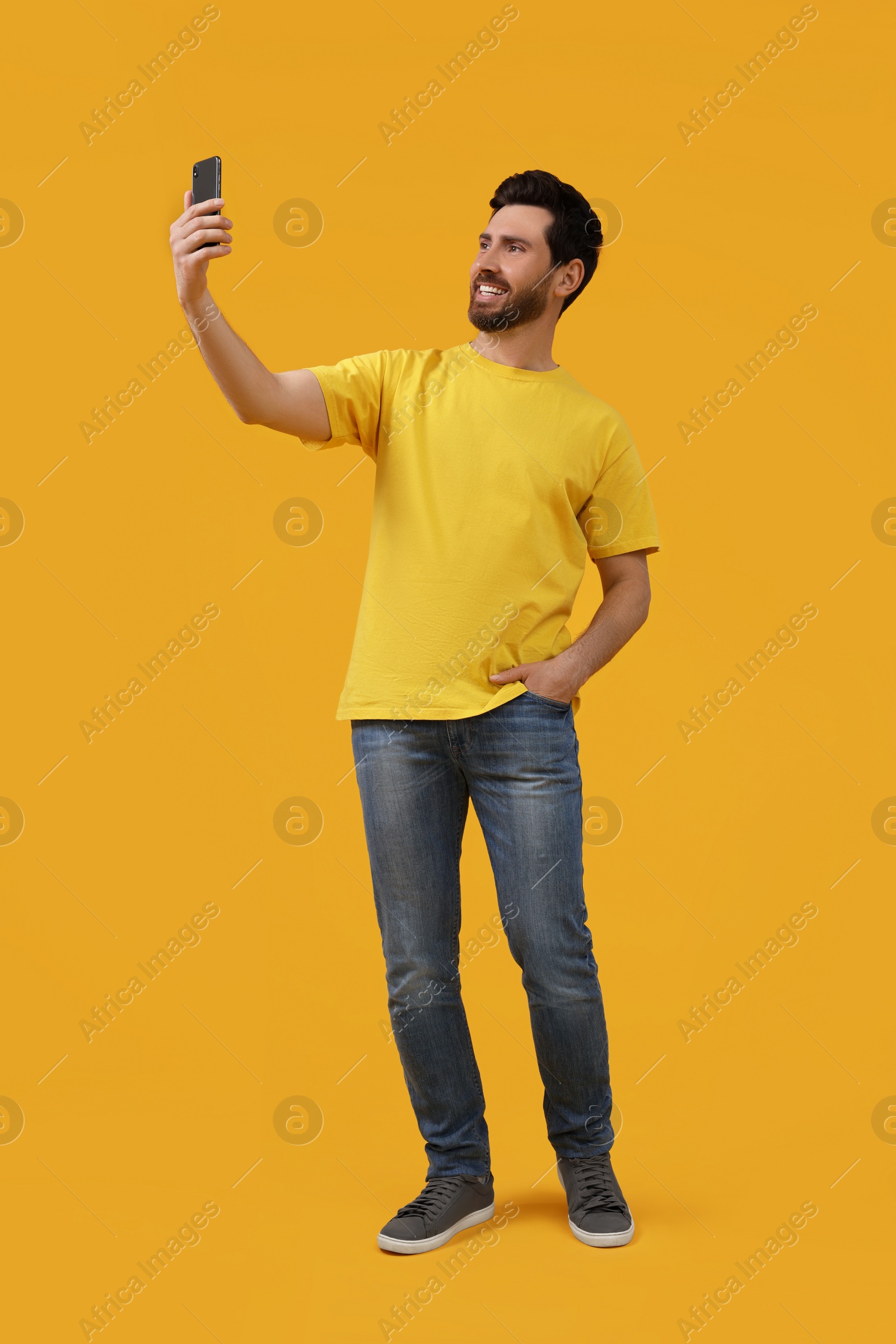 Photo of Smiling man taking selfie with smartphone on yellow background