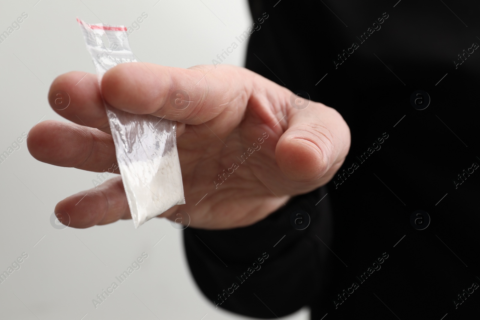 Photo of Drug addiction. Man with plastic bag of cocaine on light background, closeup