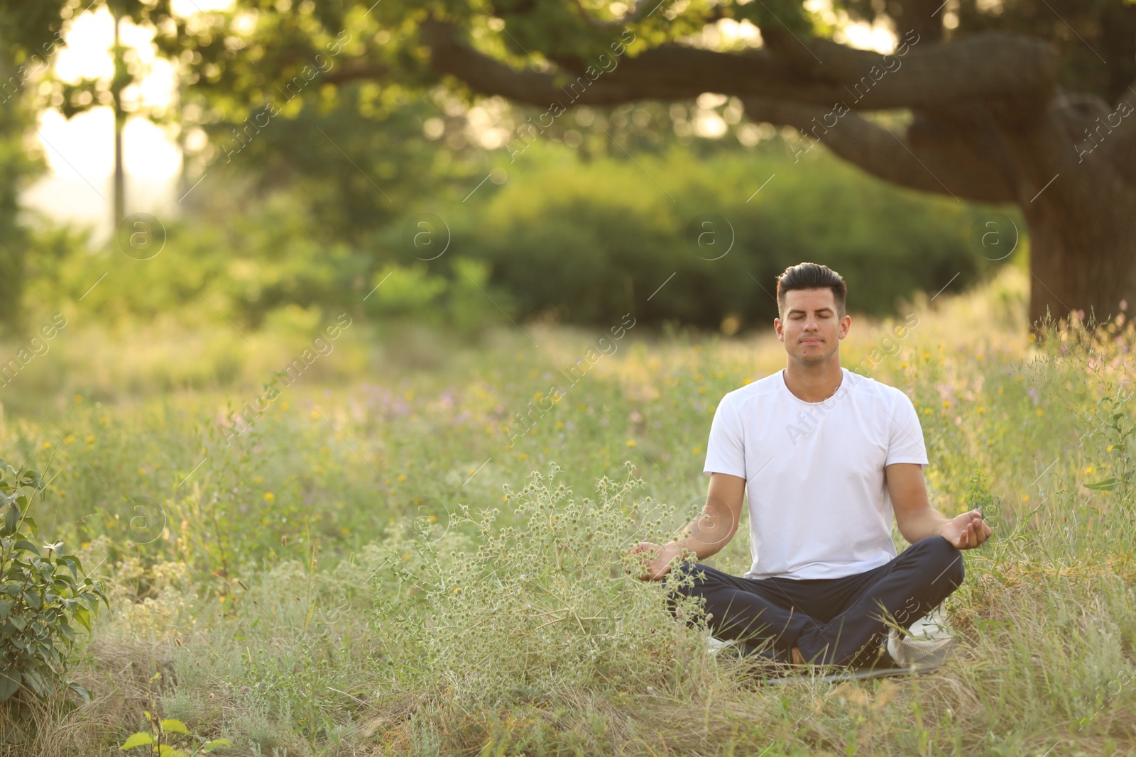 Photo of Man meditating on green grass in park, space for text