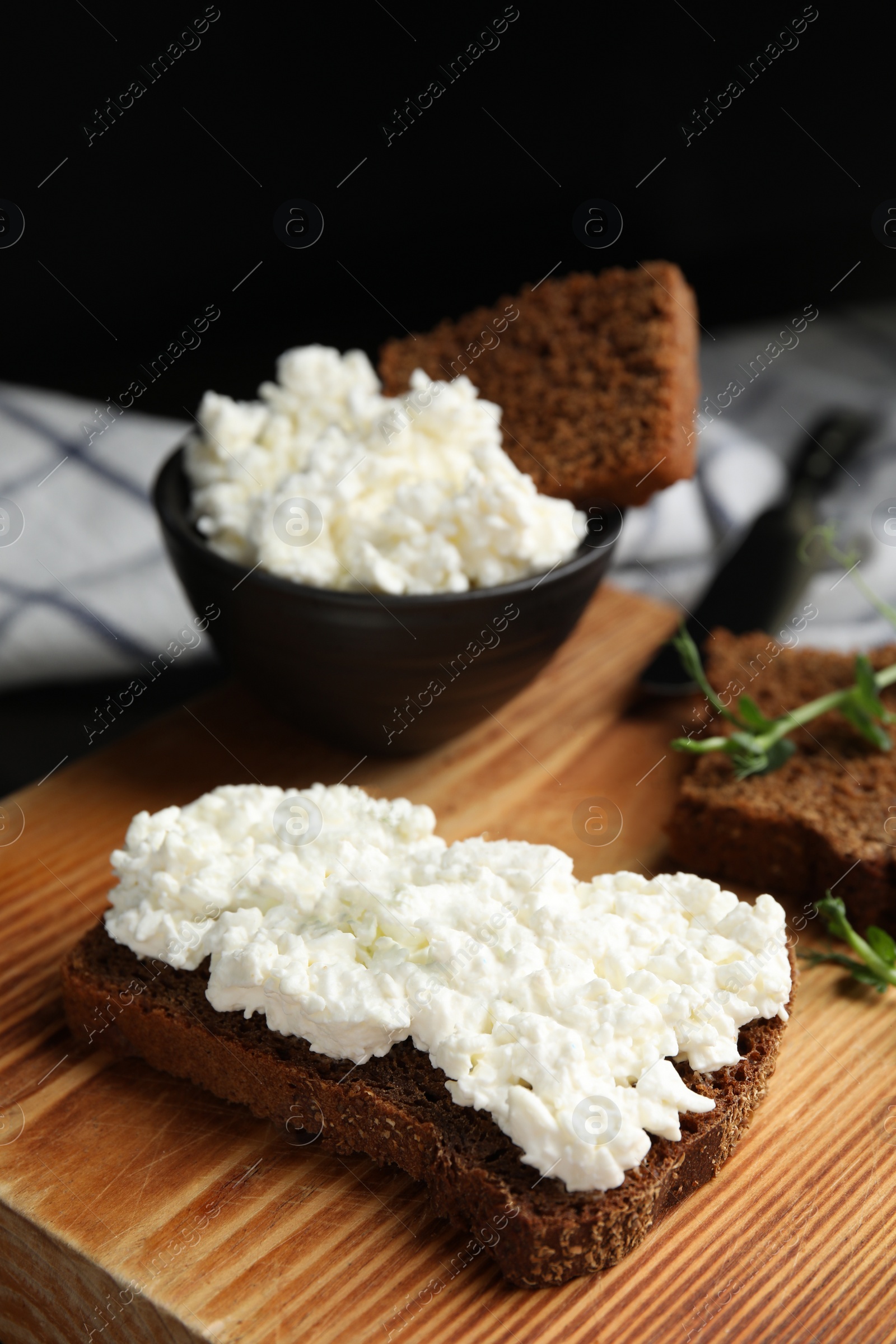 Photo of Bread with cottage cheese and microgreens on wooden board, closeup