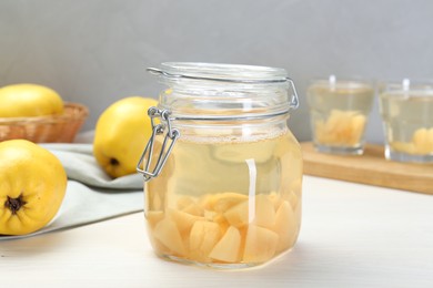 Photo of Delicious quince drink in glass jar and fresh fruits on white wooden table