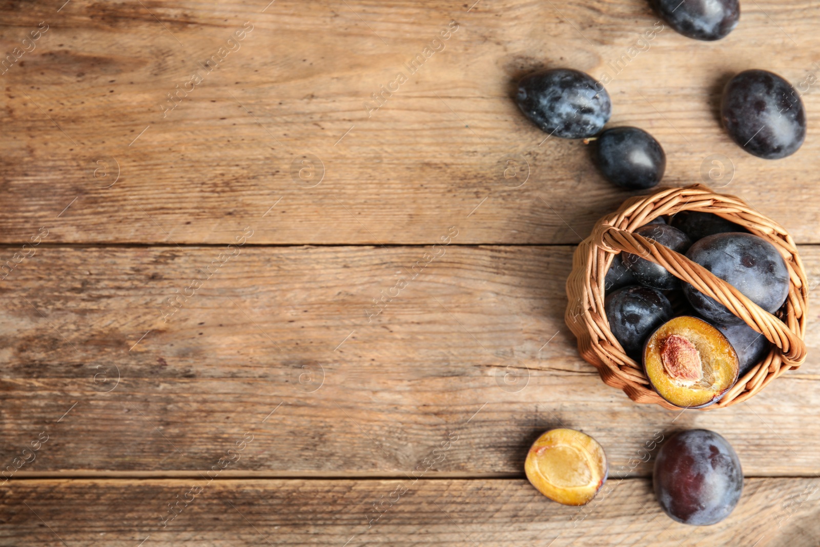 Photo of Delicious ripe plums in wicker basket on wooden table, flat lay. Space for text