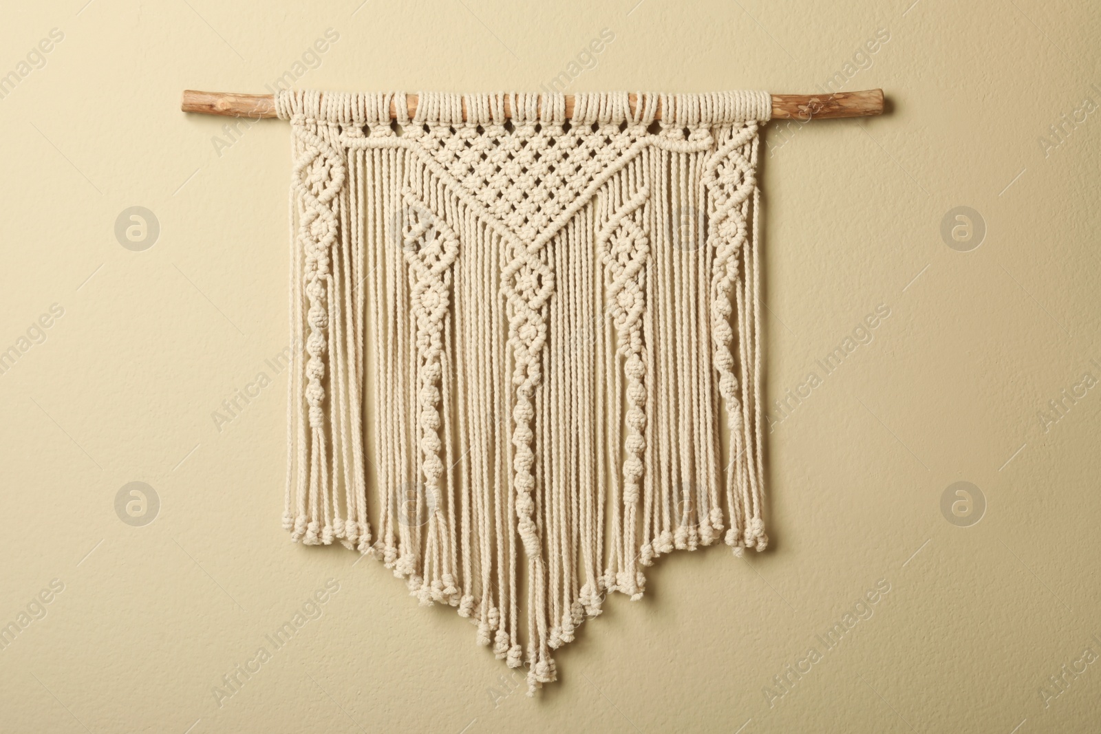 Photo of Beautiful macrame hanging on beige wall. Decorative element