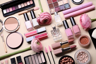 Photo of Flat lay composition with different makeup products and beautiful spring flowers on beige background