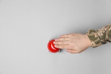 Serviceman pressing red button of nuclear weapon on light gray background, top view with space for text. War concept