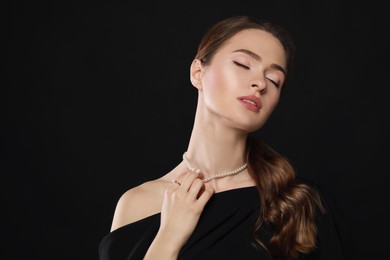 Young woman wearing elegant pearl jewelry on black background, space for text