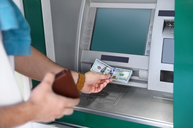 Photo of Young man taking money from cash machine outdoors, closeup