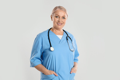 Portrait of mature doctor with stethoscope on light grey background