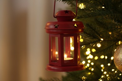 Christmas lantern with burning candle on fir tree against blurred background, closeup