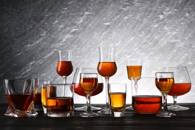 Photo of Different delicious liqueurs in glasses on dark wooden table