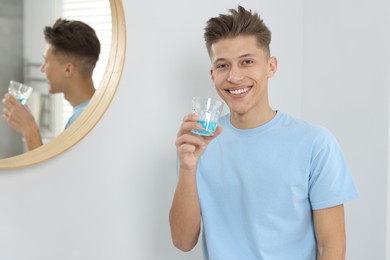 Photo of Young man with mouthwash in bathroom. Oral hygiene