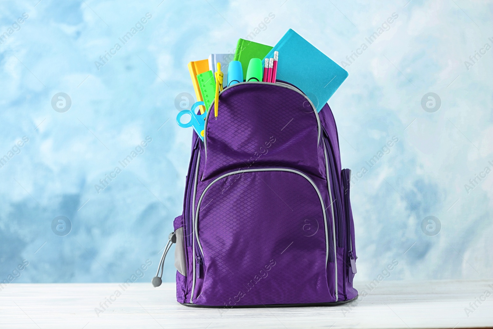 Photo of Backpack with school stationery on table against color background