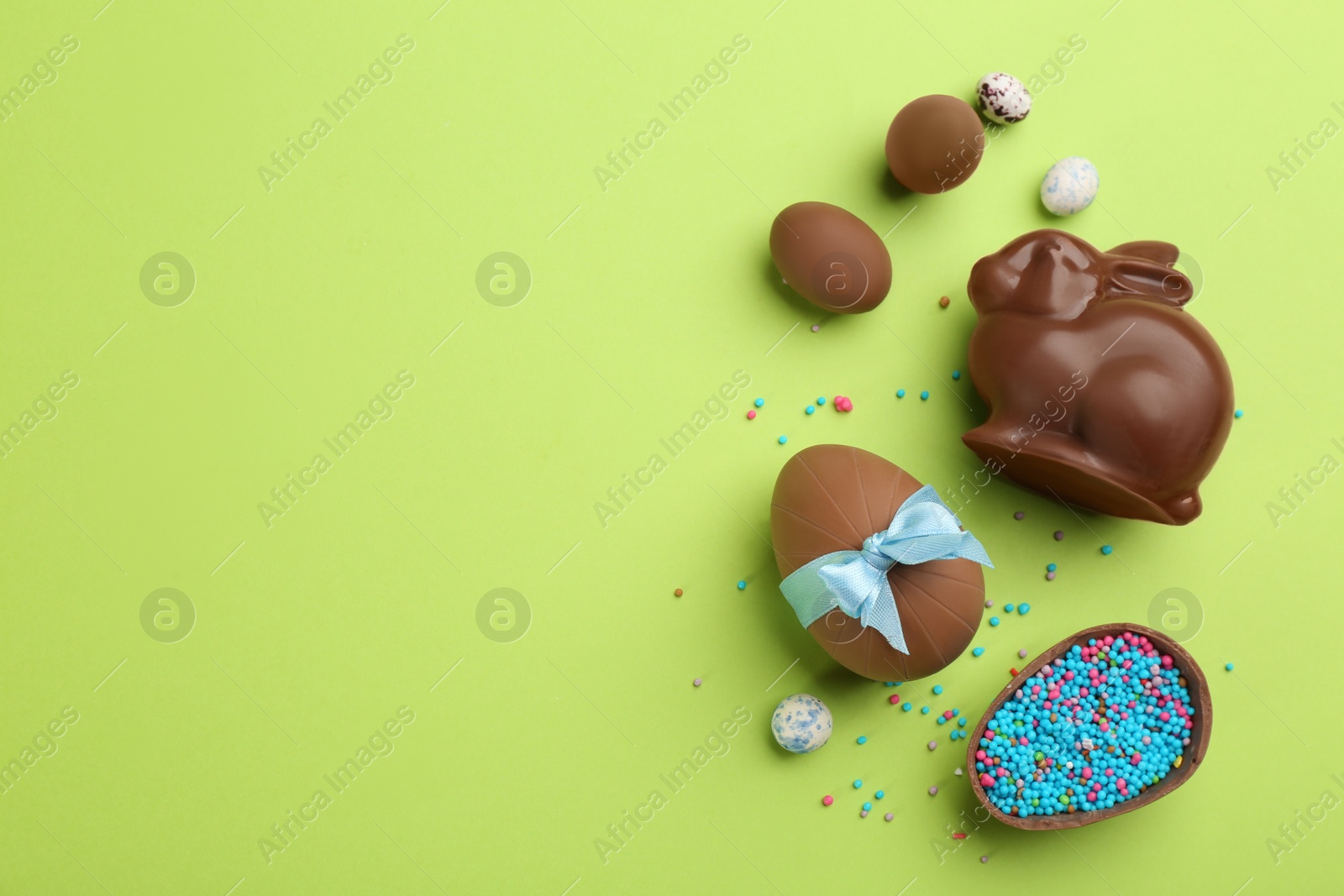 Photo of Flat lay composition with chocolate Easter bunny, eggs and candies on green background. Space for text