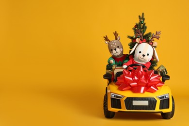 Photo of Child's electric car with toys, gift boxes and Christmas tree on orange background, space for text