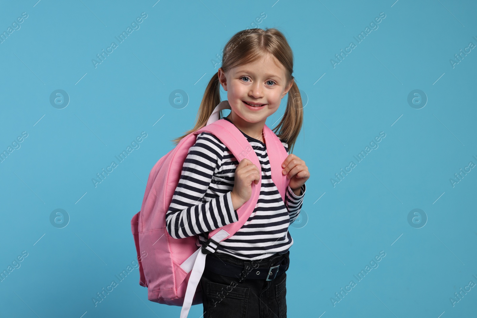 Photo of Happy schoolgirl with backpack on light blue background