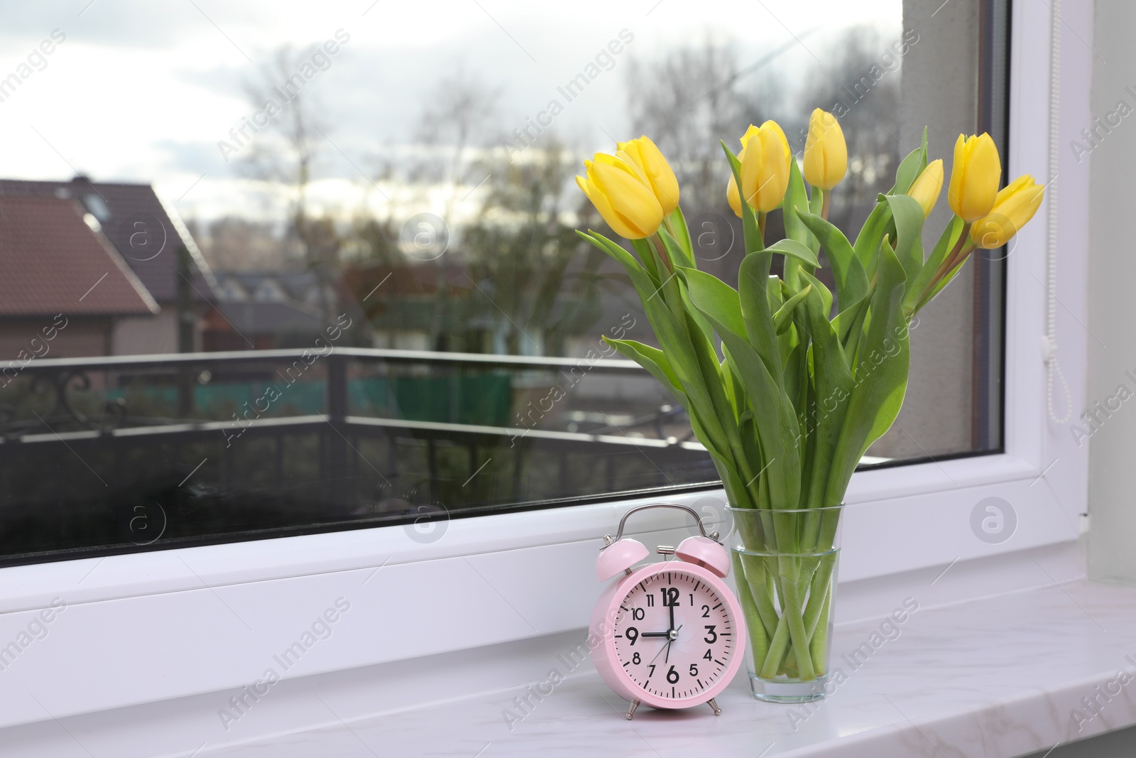 Photo of Wonderful tulips and alarm clock on window sill indoors, space for text. Spring atmosphere