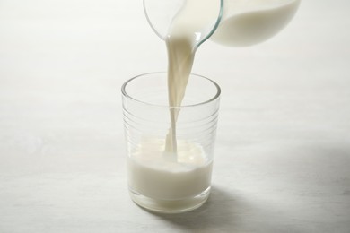 Photo of Pouring milk into glass on white table