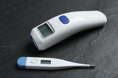 Photo of Non-contact infrared and digital thermometers on black slate background