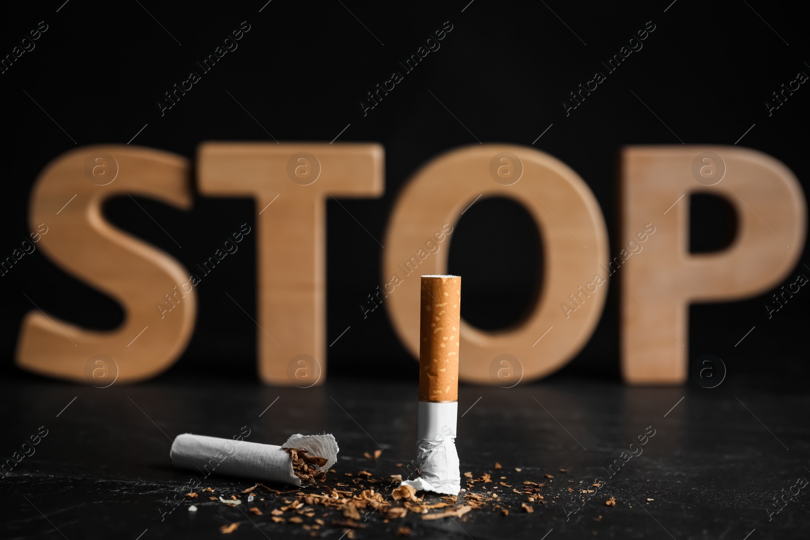 Photo of Broken cigarette near word Stop on black table. Quitting smoking concept