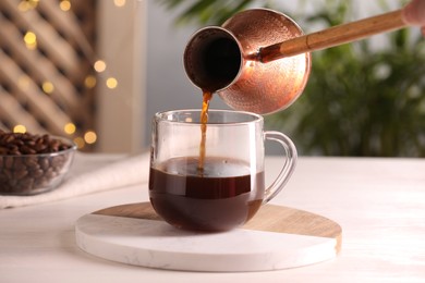 Photo of Pouring aromatic coffee from cezve into cup at white wooden table, closeup