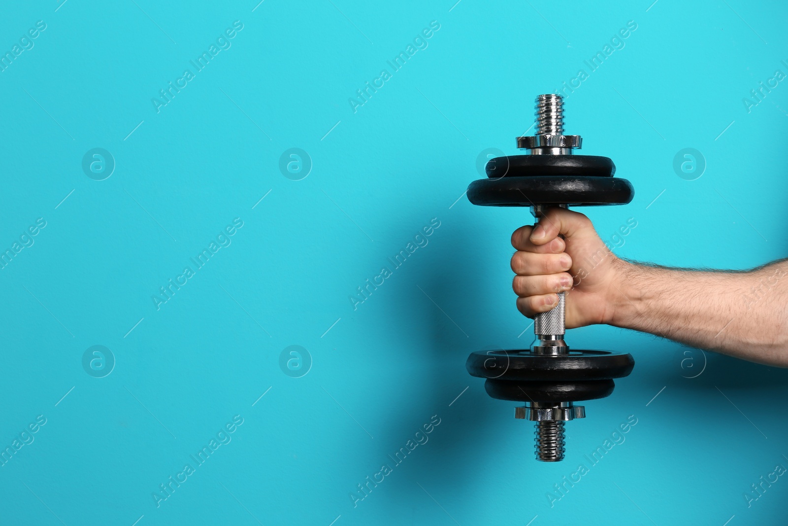 Photo of Male athlete holding metal dumbbell on color background. Space for text