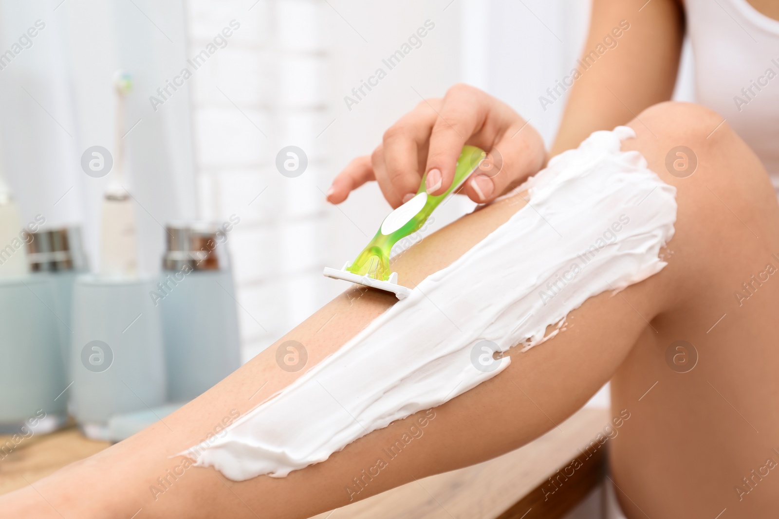 Photo of Beautiful young woman shaving leg at home. Space for text