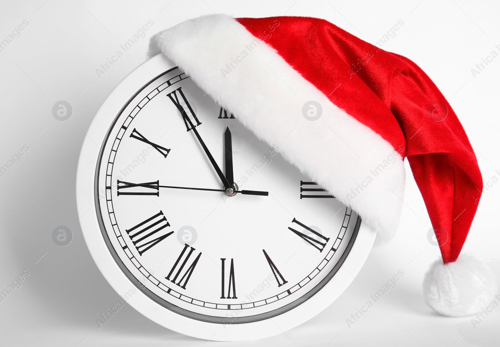 Photo of Clock with Santa hat showing five minutes until midnight on white background. New Year countdown