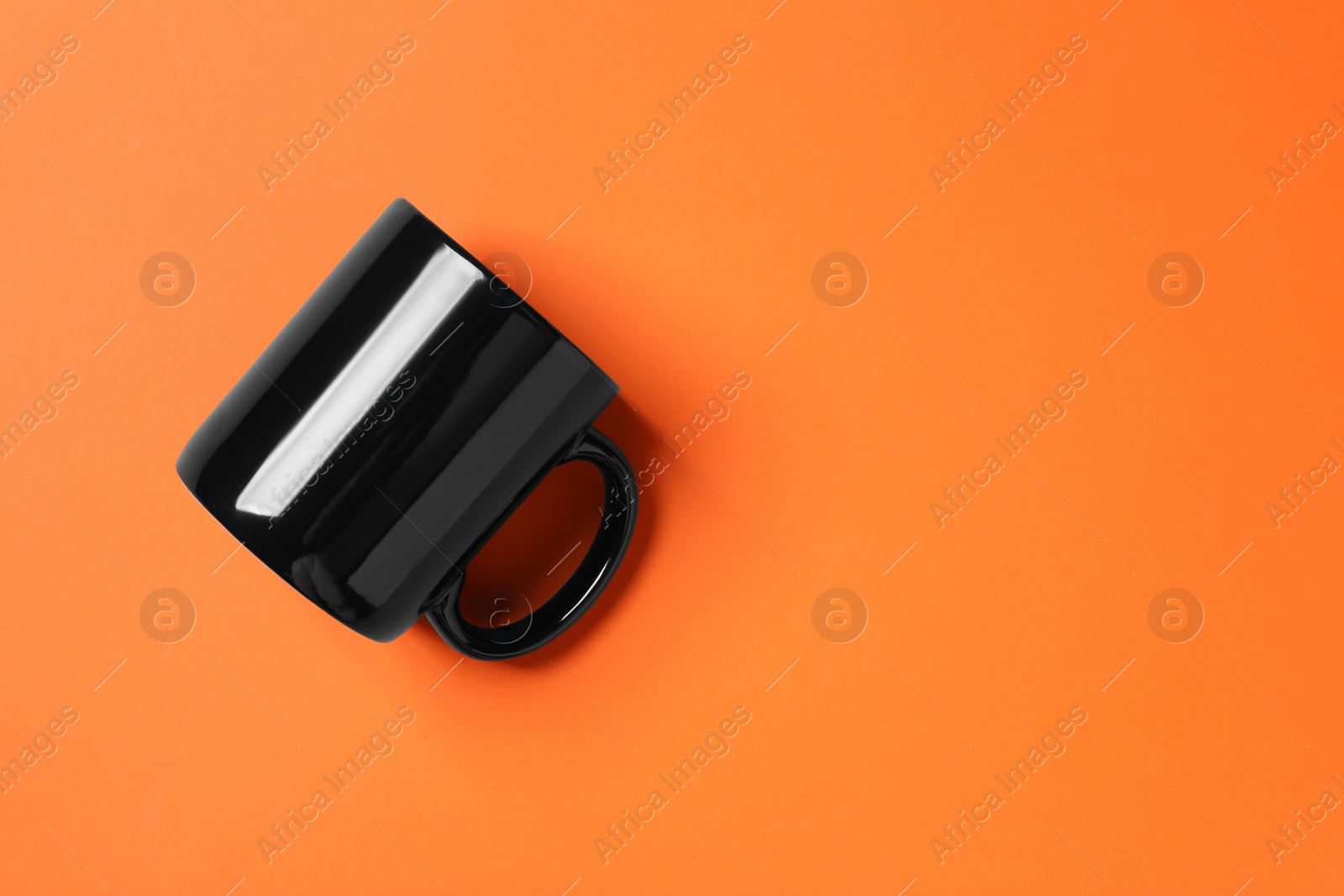 One black ceramic mug on orange background, top view. Space for text Photo of One black ceramic mug on orange background, top view. Space for text