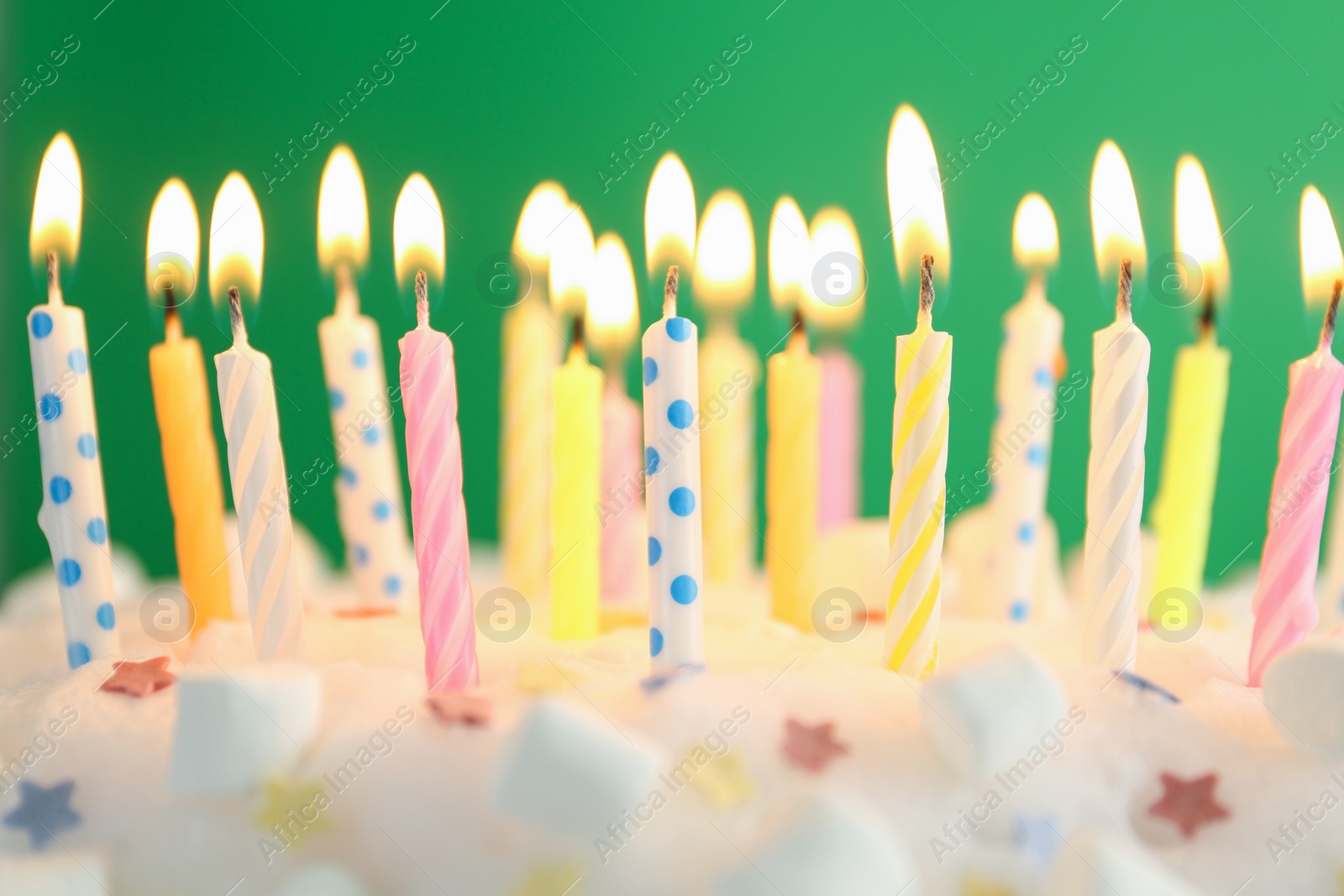 Photo of Birthday cake with burning candles on green background, closeup