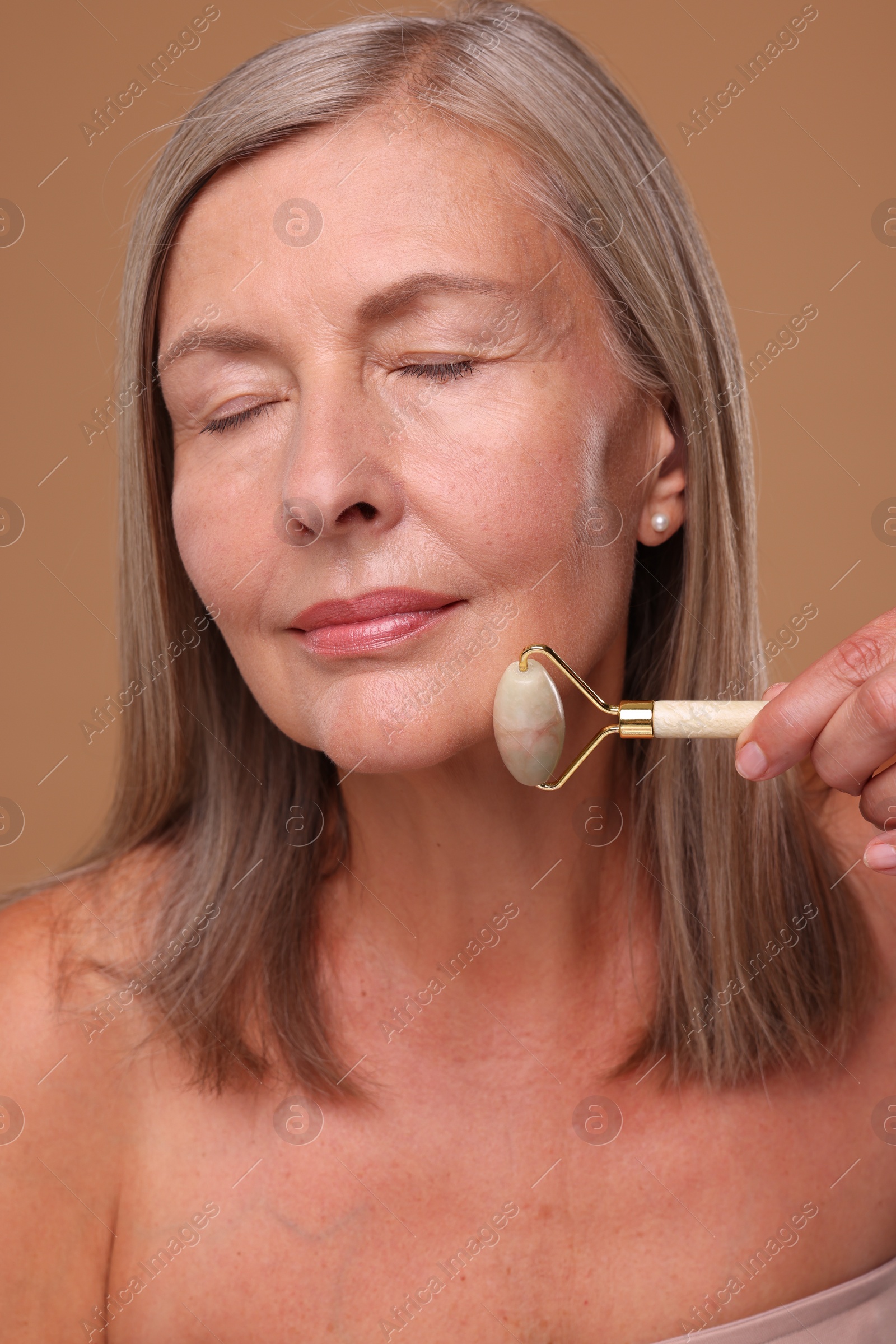 Photo of Woman massaging her face with jade roller on brown background