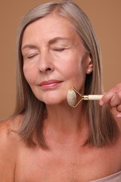 Woman massaging her face with jade roller on brown background
