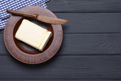 Photo of Clay plate with butter and knife on black wooden table, top view. Space for text