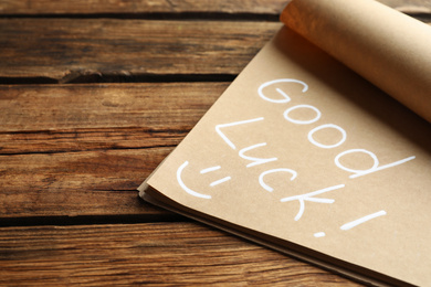 Photo of Notebook with phrase GOOD LUCK and funny face on wooden background, closeup