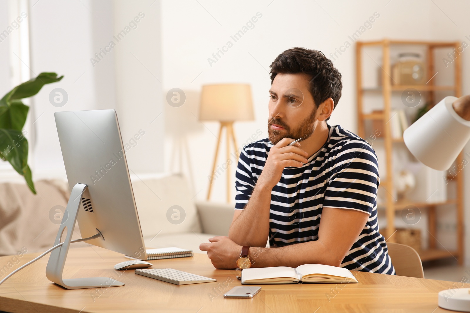 Photo of Home workplace. Man working with computer at wooden desk in room