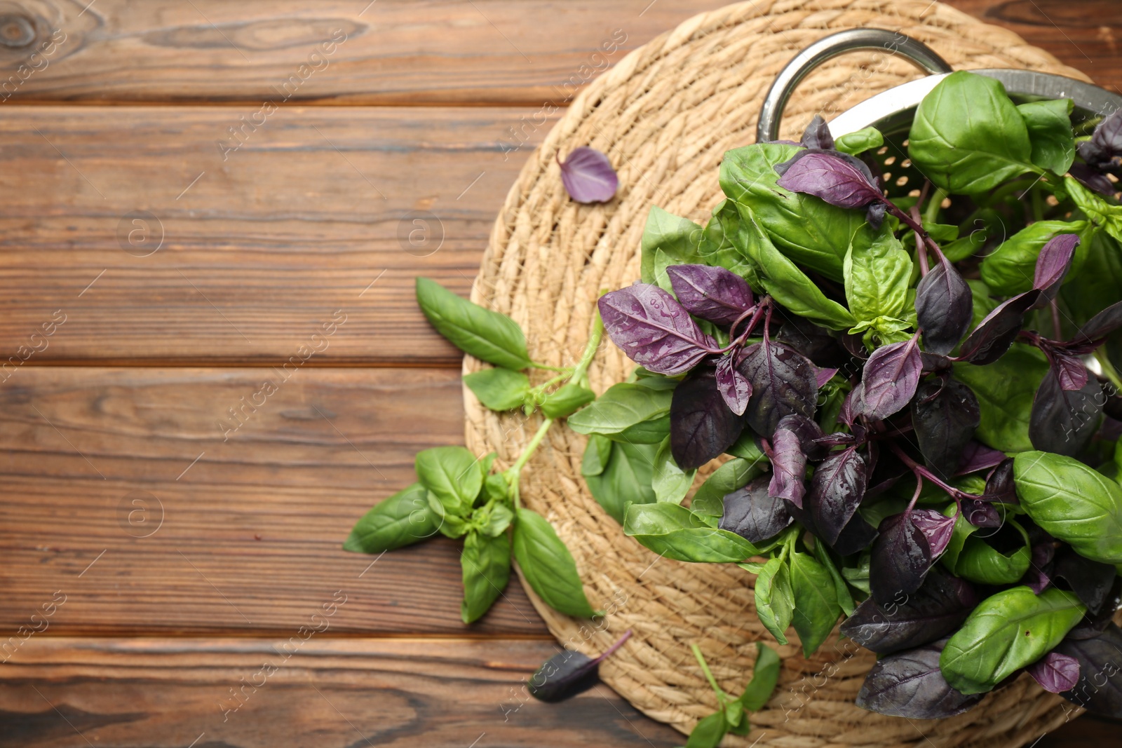 Photo of Metal colander with different fresh basil leaves on wooden table, top view. Space for text