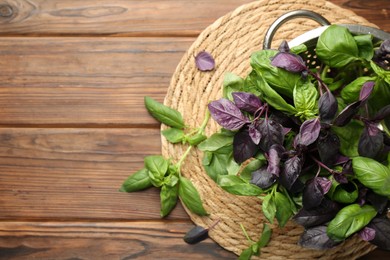 Metal colander with different fresh basil leaves on wooden table, top view. Space for text