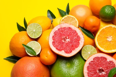 Photo of Different ripe citrus fruits with green leaves on yellow background, flat lay