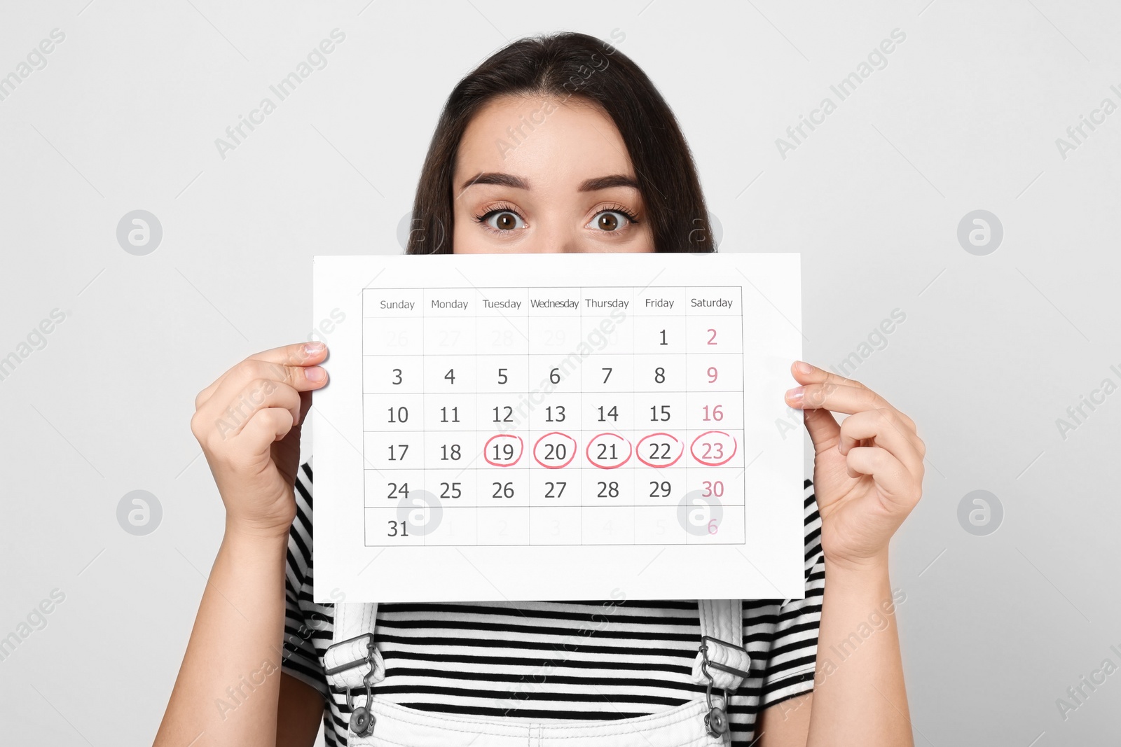 Photo of Young woman holding calendar with marked menstrual cycle days on light background