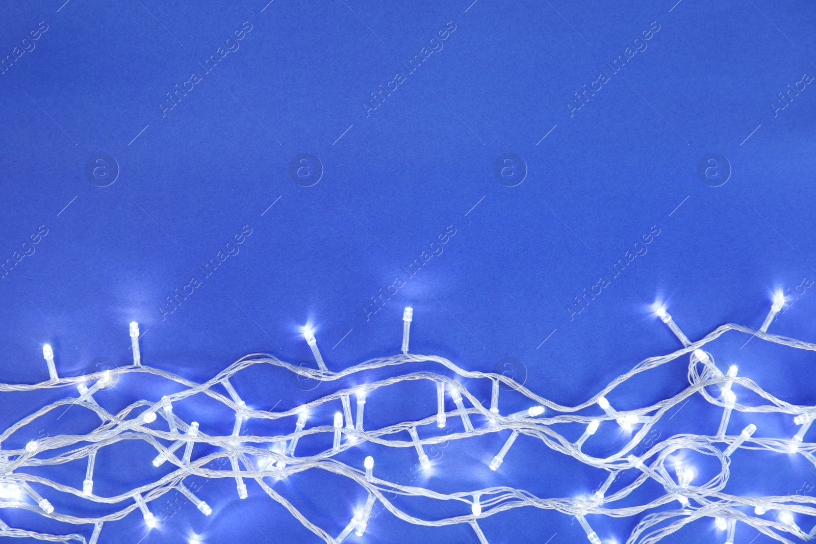 Photo of Glowing Christmas lights on color background, top view