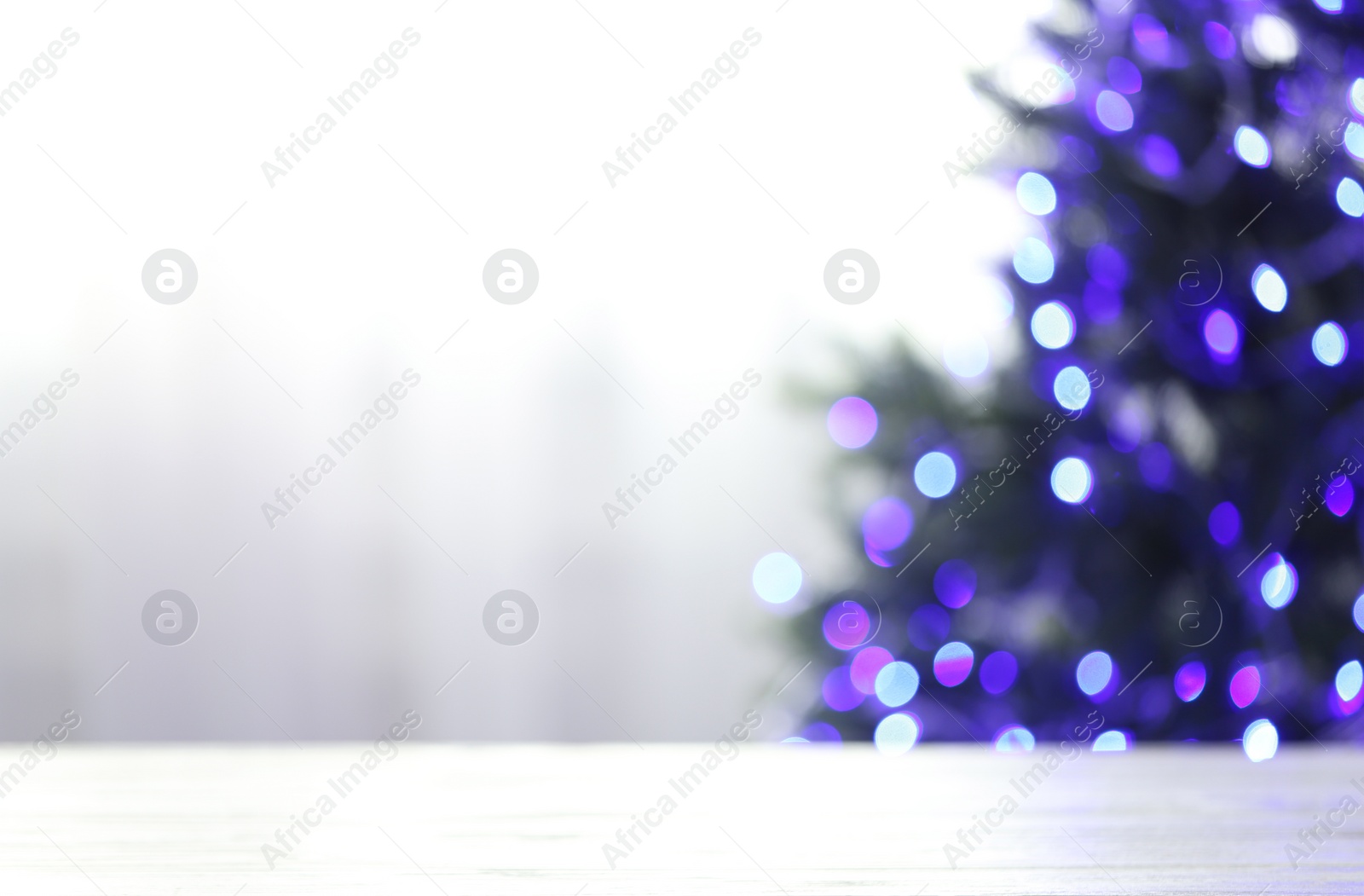 Photo of Empty table and blurred fir tree with violet Christmas lights on background, bokeh effect. Space for design