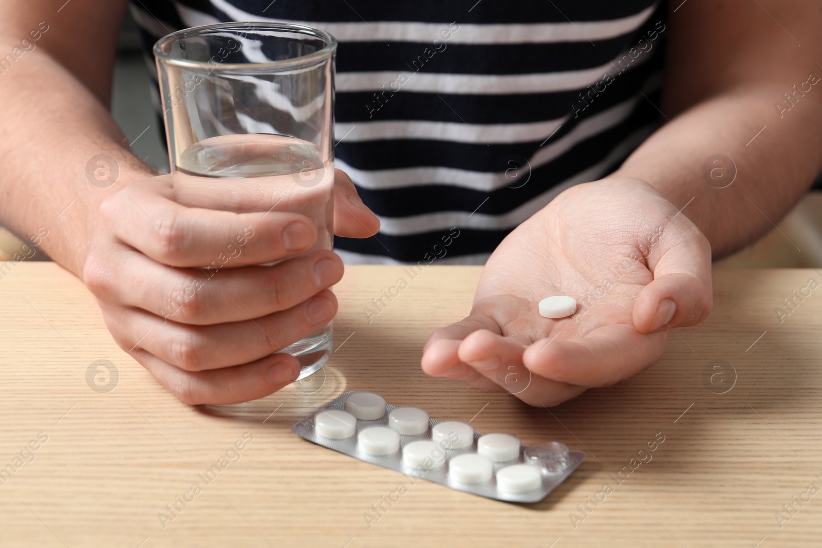 Photo of Man with glass of water and pill at wooden table, closeup