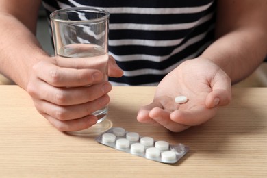 Man with glass of water and pill at wooden table, closeup