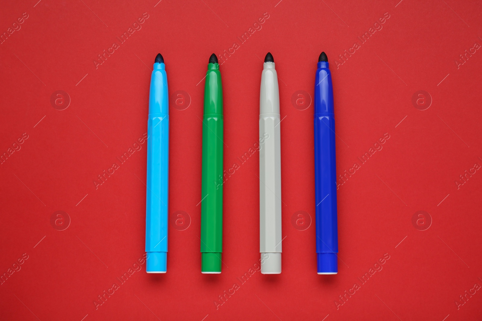 Photo of Different colorful markers on red background, flat lay