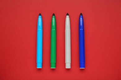Photo of Different colorful markers on red background, flat lay