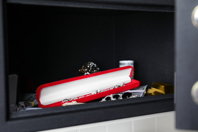 Photo of Open black steel safe with money, gold bars and jewelry on shelf