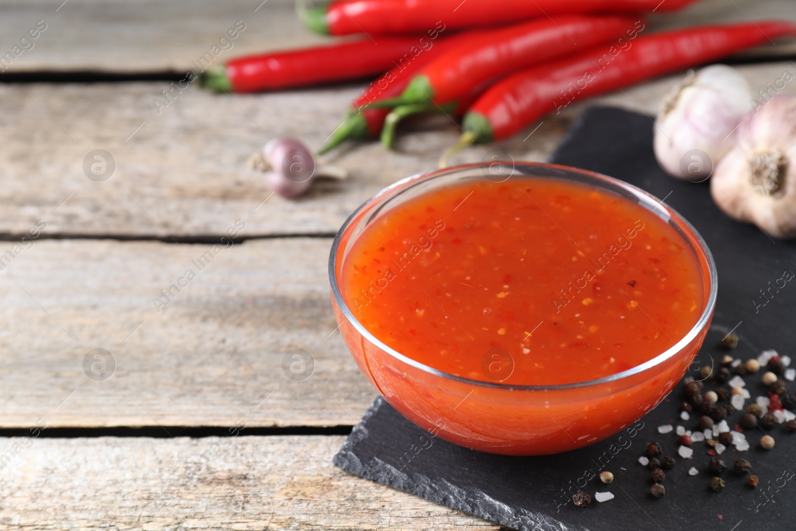 Photo of Spicy chili sauce in bowl and ingredients on wooden table, closeup. Space for text