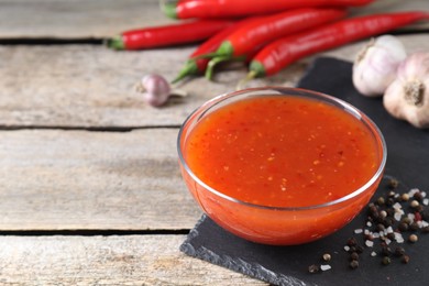 Photo of Spicy chili sauce in bowl and ingredients on wooden table, closeup. Space for text