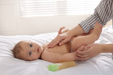 Photo of Mother massaging her cute baby with oil on bed at home, closeup