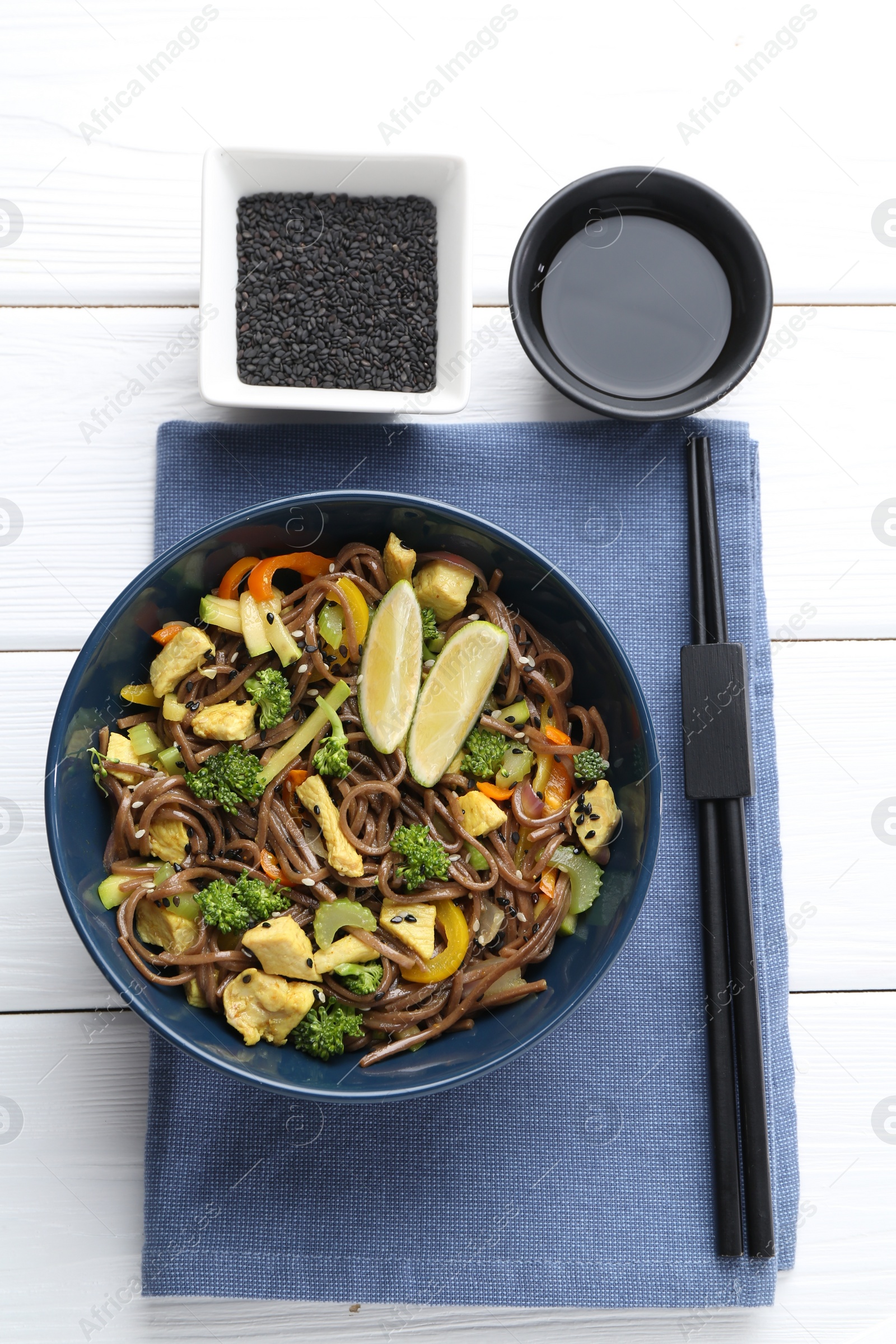 Photo of Stir-fry. Delicious cooked noodles with chicken and vegetables in bowl served on white wooden table, flat lay